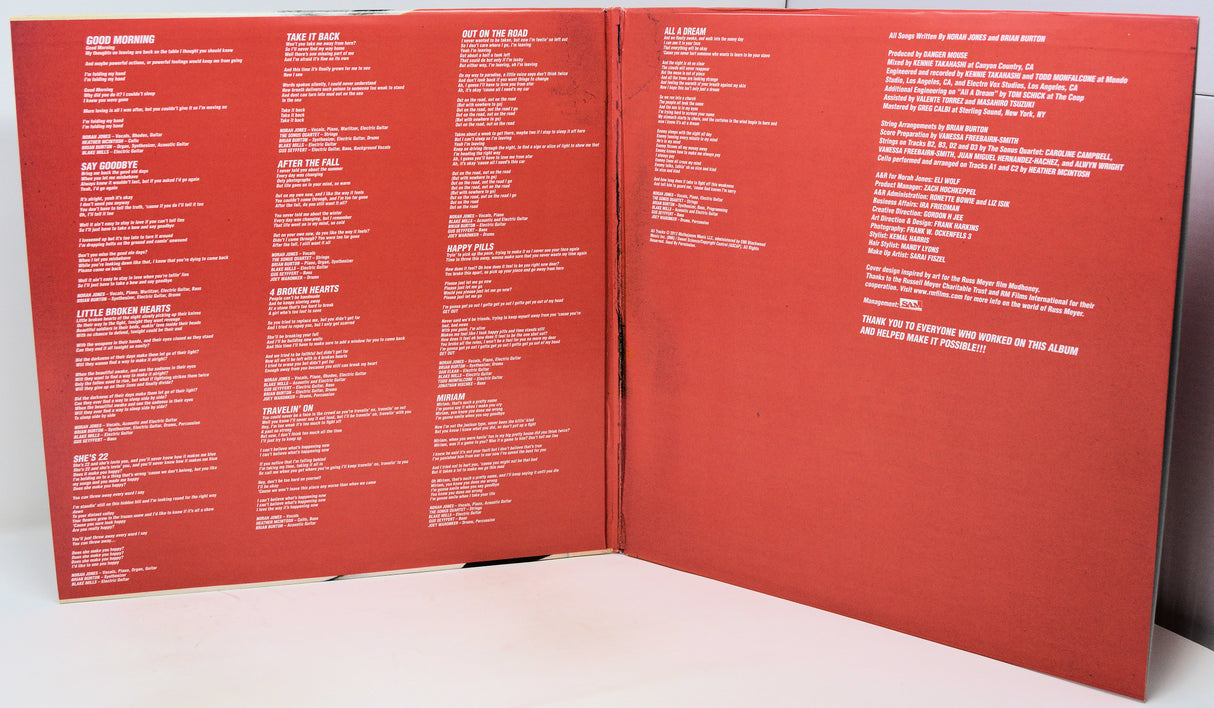 An open vinyl record sleeve or booklet showing the back cover with dense white track listings and text on a red background, photographed on a white surface.