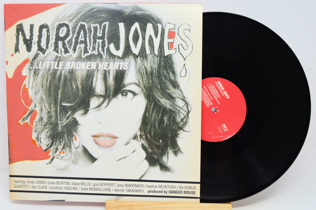 Norah Jones - 'A Little Broken Hearts' vinyl record LP with its illustrated album cover sleeve and a black vinyl record partially visible behind it on a white background.