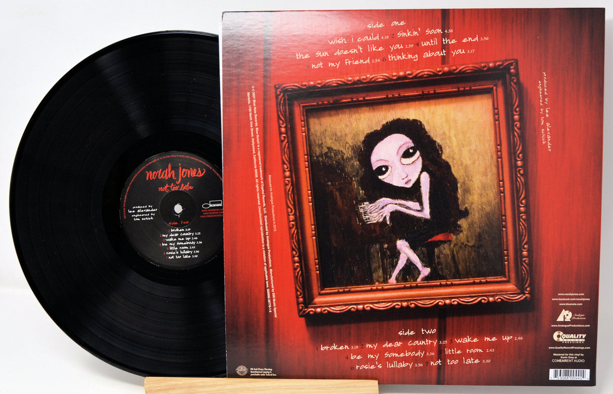 A vinyl record partially pulled from its album sleeve, showing the black disc on the left and the back cover artwork on the right. The sleeve features a red wood-grain background with a framed painting of a pale figure and white handwritten text.