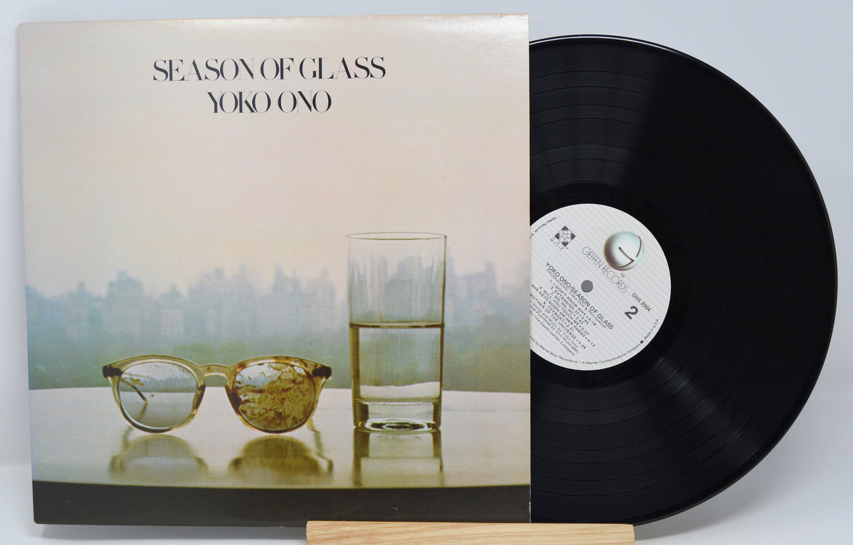 A vinyl record of 'Season of Glass' by Yoko Ono with the album cover visible. The cover features a photograph of a glass of water and a cityscape.