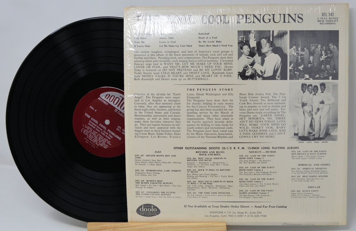 Vinyl record with its cover featuring text and images of people, on a light gray background.