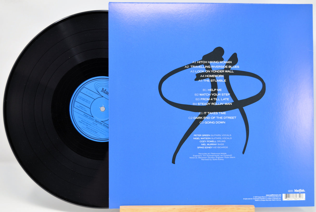 Vinyl record partially pulled from its blue sleeve, showing the black record, blue center label, and back cover artwork with white track listing text and a black abstract figure graphic on a bright blue background.
