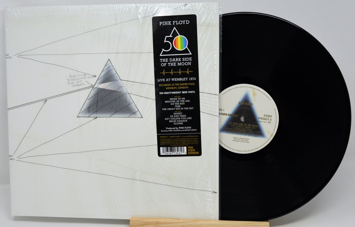 Pink Floyd 'The Dark Side of the Moon' 12-inch vinyl record shown in its shrink-wrapped outer sleeve with the black LP record partially pulled out, displayed on a small wooden stand against a light gray background.