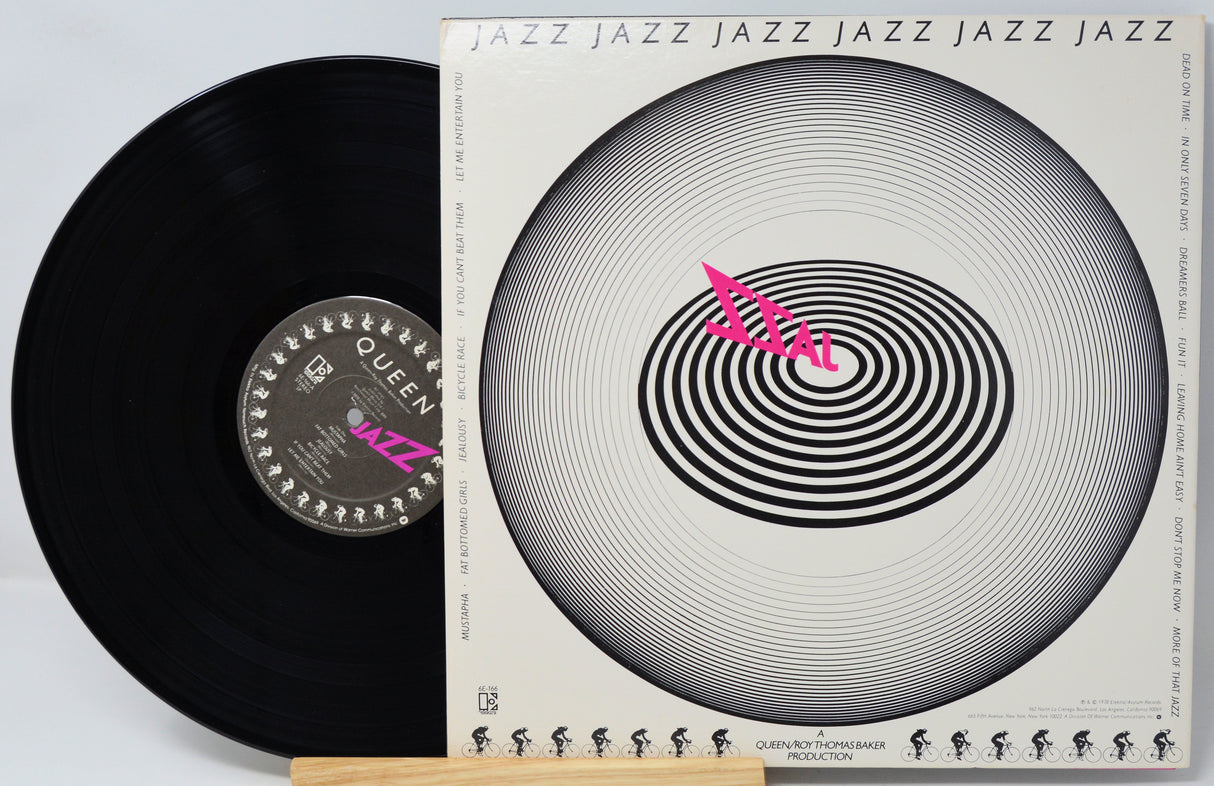 A vinyl record and its album cover for Queen's 'Jazz' album, displayed on a light wood stand against a white background.