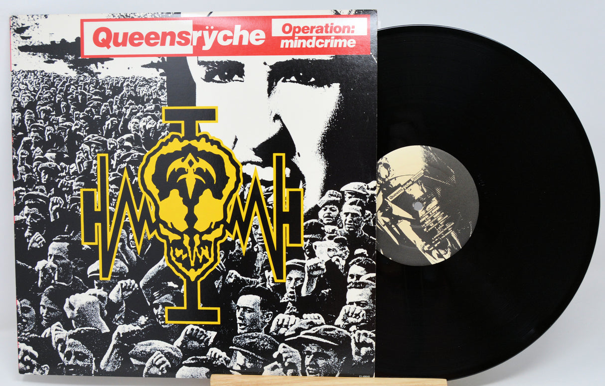 Queensyche's Operation: Mindcrime vinyl record album with the black LP partially pulled from the sleeve, photographed on a light gray background.
