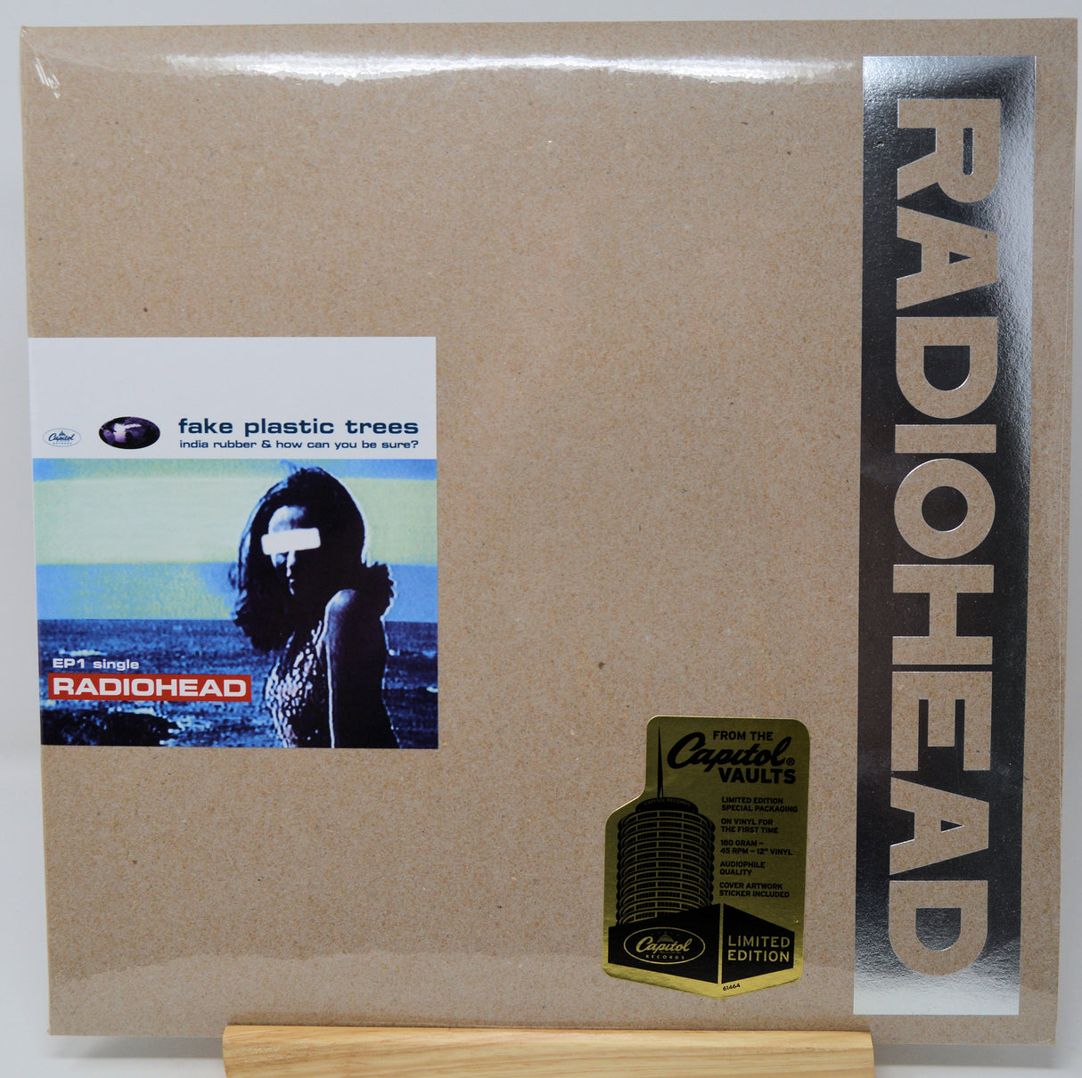 Radiohead 'Fake Plastic Trees' limited edition vinyl record cover, sealed in plastic with a gold Crested Vaults Vaulted Edition sticker, displayed on a wooden stand.