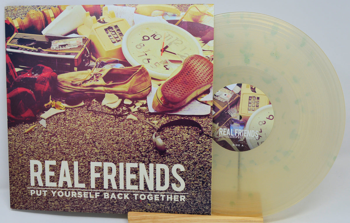 Real Friends vinyl record album with the LP partially pulled from the sleeve, showing a translucent pale green record and cover art featuring a collage of objects on a textured ground with the title 'REAL FRIENDS PUT YOURSELF BACK TOGETHER'.