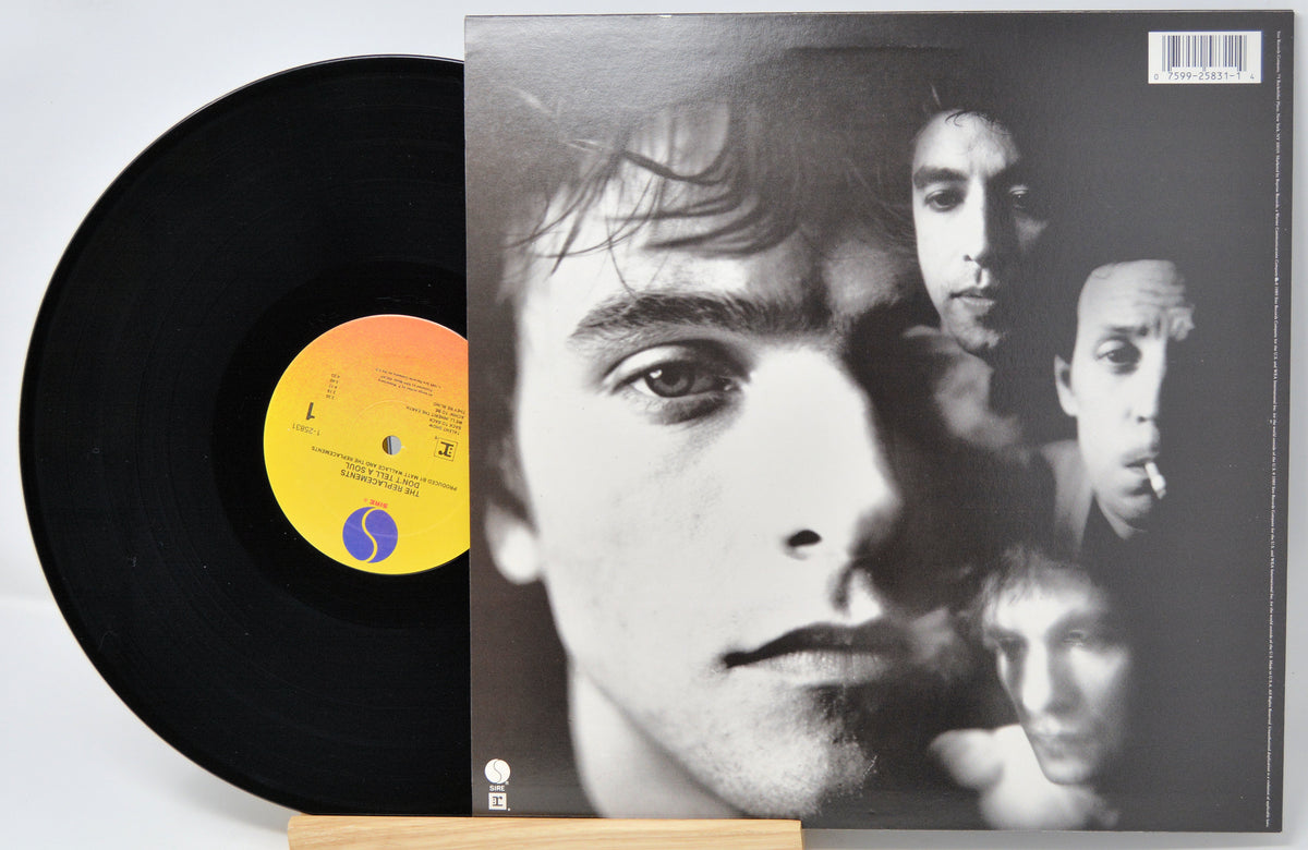 A vinyl record partially pulled from its sleeve, showing a black disc with a yellow and orange center label beside a black-and-white album cover featuring a close-up portrait collage.