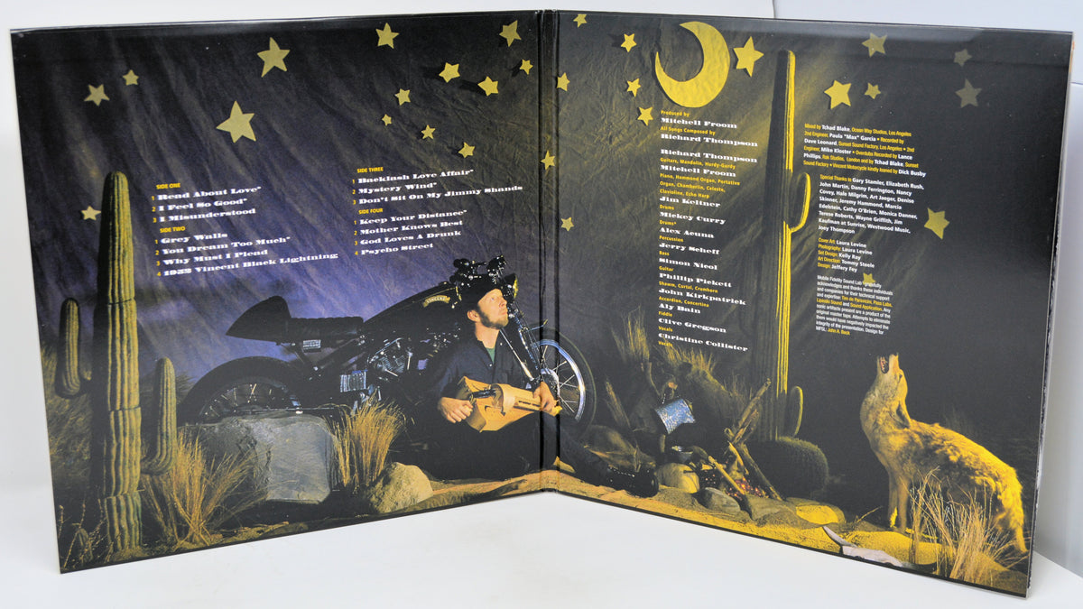 An open vinyl record sleeve or booklet displaying printed desert night artwork with a motorcycle, cactus, moon, stars, and a wolf, alongside song lists on both sides.