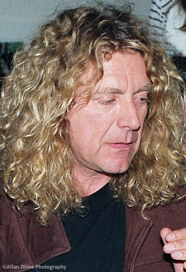 Photo of Robert Plant with curly blonde hair wearing a brown jacket and black shirt.