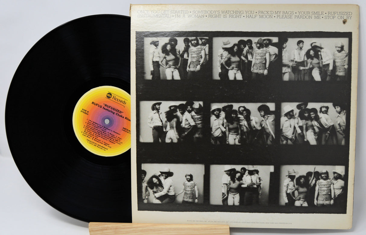 Vinyl record with a black cover featuring black and white photos of a band, on a light gray background.