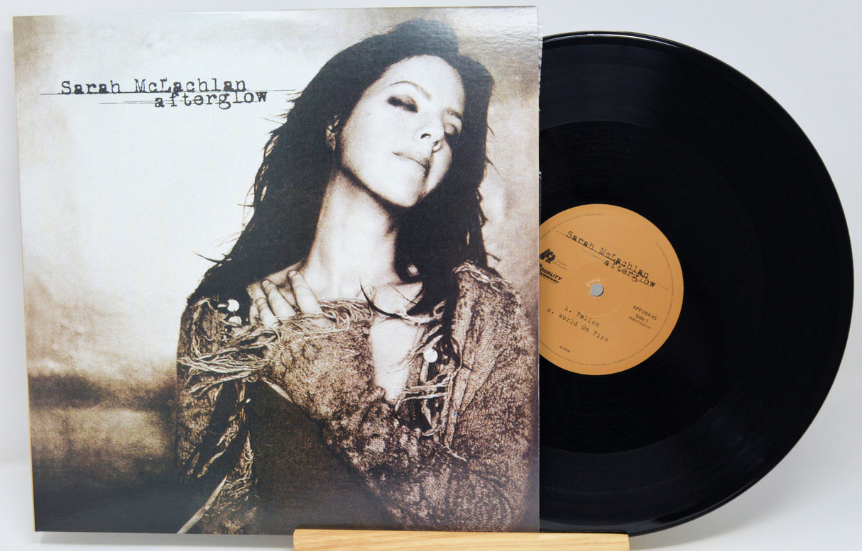 A vinyl record album for Sarah McPhaul's album 'atlonglow' shown with its illustrated cover sleeve and a black LP record partially pulled out, resting on a small wooden stand against a light gray background.