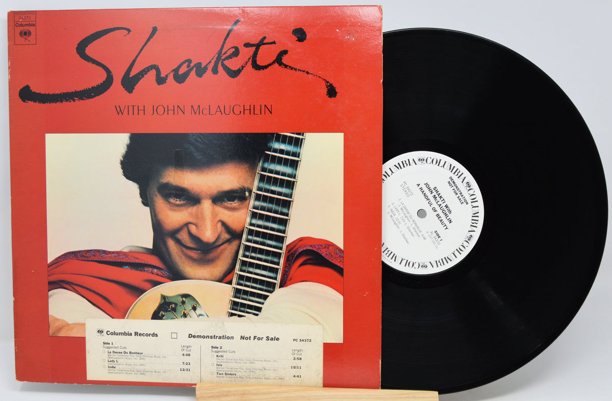 Shakti with John McLaughlin vinyl record album shown with its red cover and a black LP record partially pulled out, photographed against a light gray background.
