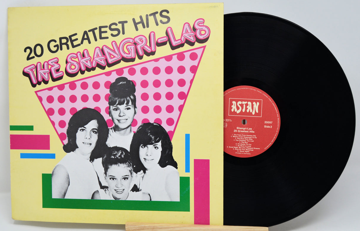 Vinyl record with cover featuring '20 Greatest Hits' by The Shangri-Las on a yellow background.