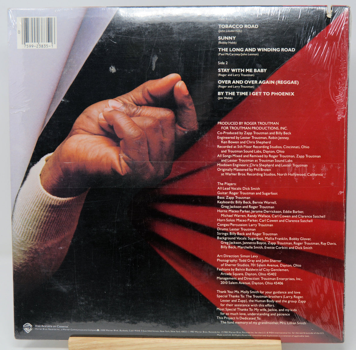 Vinyl record sleeve with a hand holding red fabric and tracklist on a white background