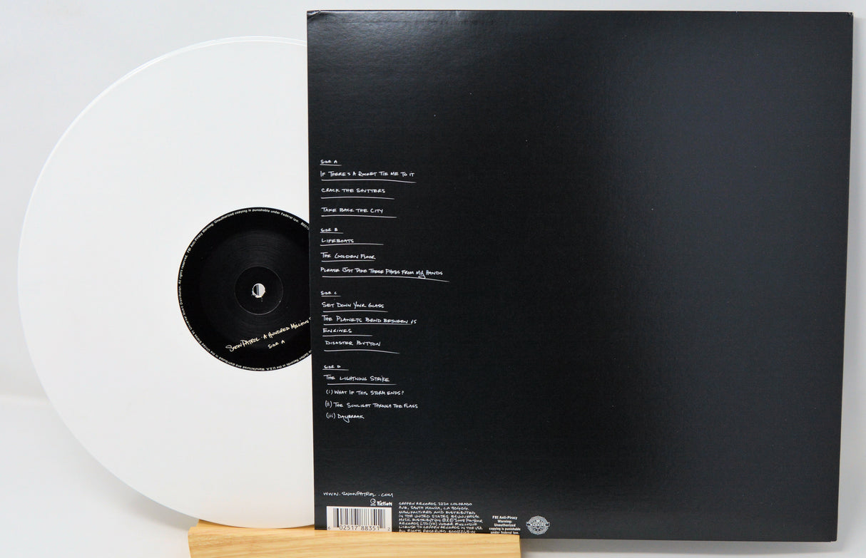 A vinyl record partially pulled from its black outer sleeve, photographed on a white background with a small wooden stand visible at the bottom.