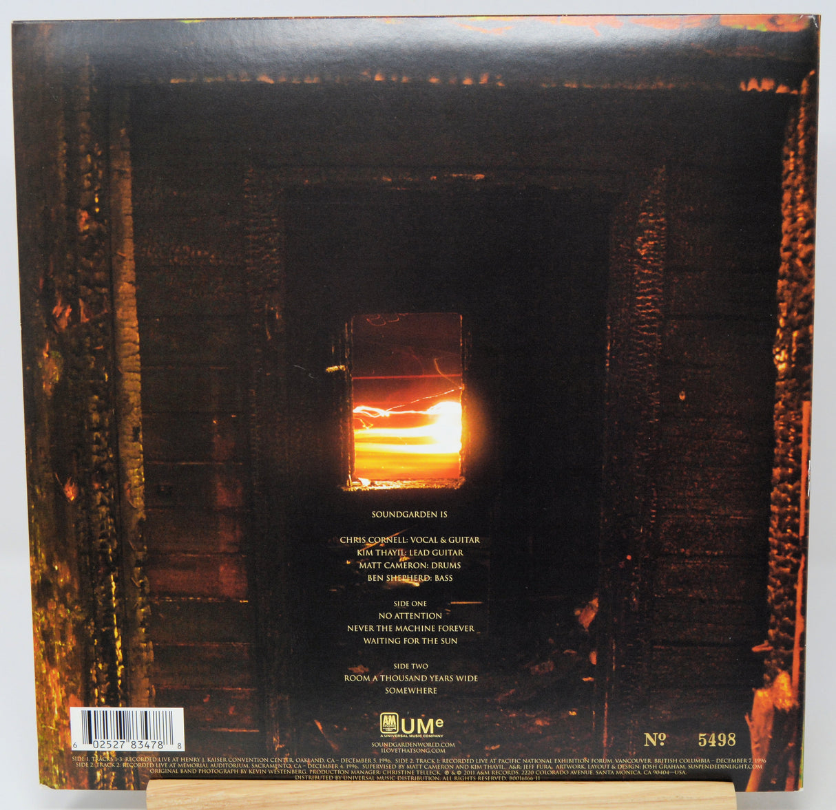 The back cover of a vinyl record for Soundgarden's album 'Showbizgenial', featuring a dark, fiery scene with a glowing orange window and tracklist text, displayed on a wooden stand.