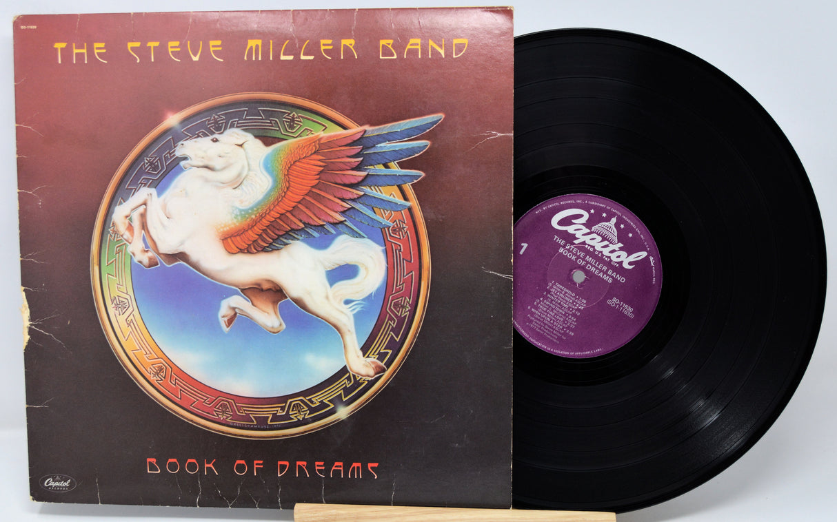 Vinyl record and cover of 'Book of Dreams' by The Steve Miller Band on a white background