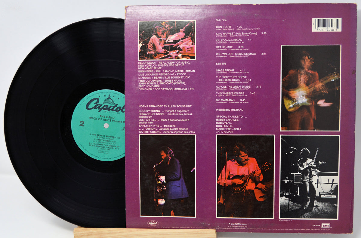 A vinyl record shown with its back cover standing upright behind it. The black record on the left has a green Capitol label, and the purple back cover features multiple small concert photos and printed track listings.