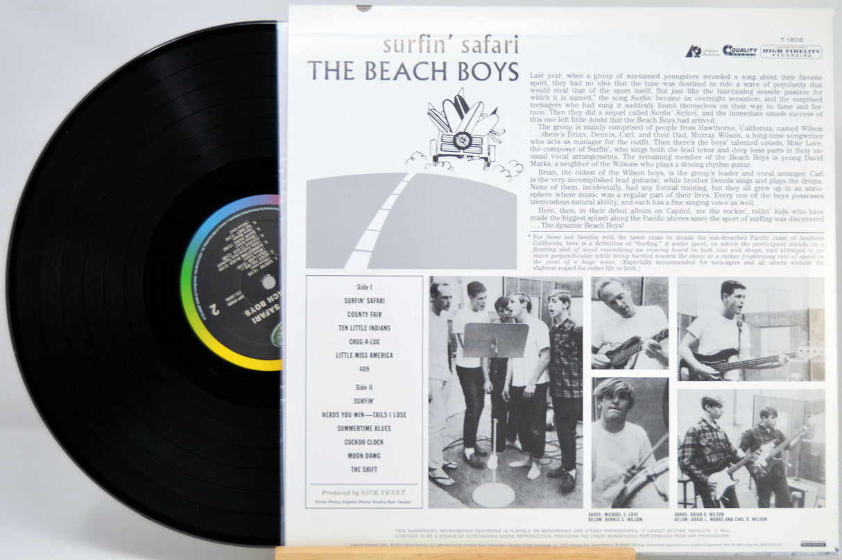Vinyl record album shown with the black LP partially pulled from the printed inner sleeve. The sleeve features the title 'surfin' safari', the band name 'THE BEACH BOYS', track list, and black-and-white photos of the band members.