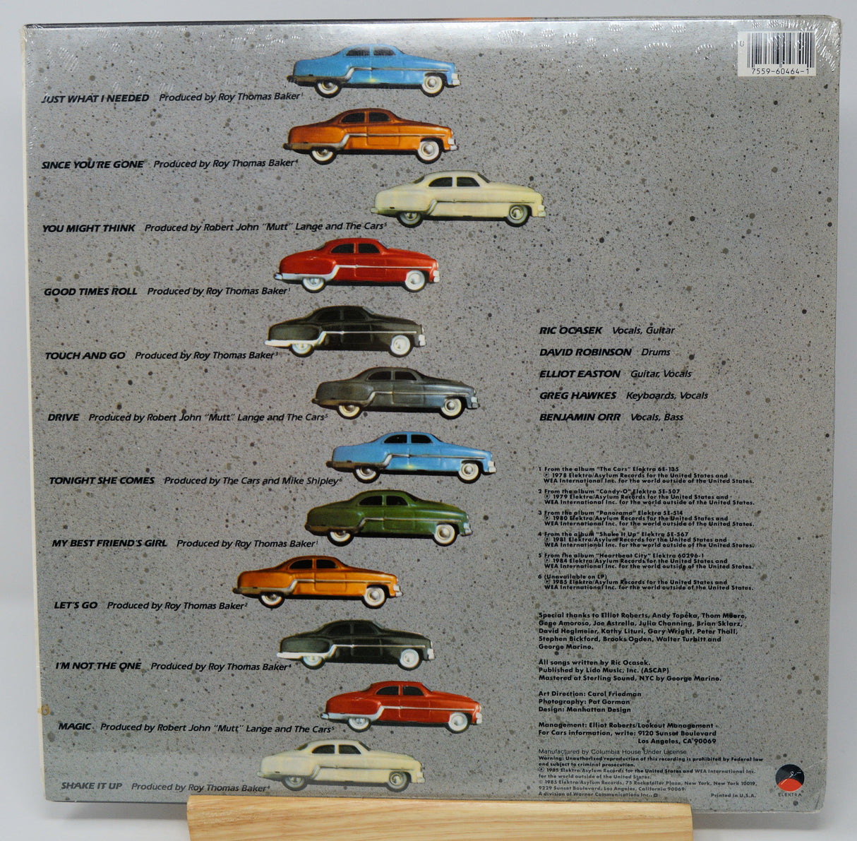 The back cover of a vinyl record sleeve for Ray Thomas Ballard's album 'Just What I Need', displayed on a small wooden stand. The cover features a textured gray background with a row of illustrated vintage cars in various colors (blue, orange, yellow, red, green, black, white) above a tracklist and credits.