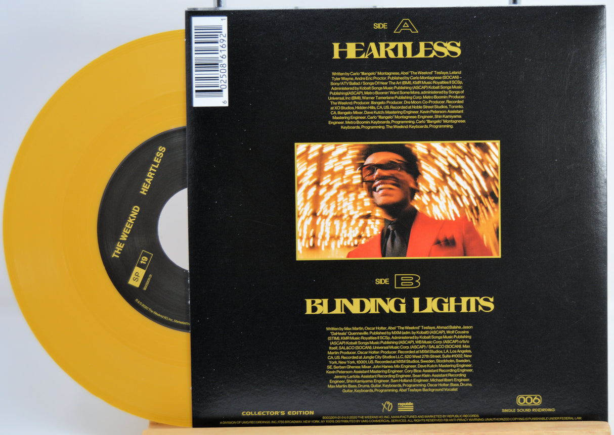 The Weekend Heartless variant #6 7 Inch Vinyl record with a black Back cover featuring a person wearing sunglasses and a red jacket, and a yellow record inside.
