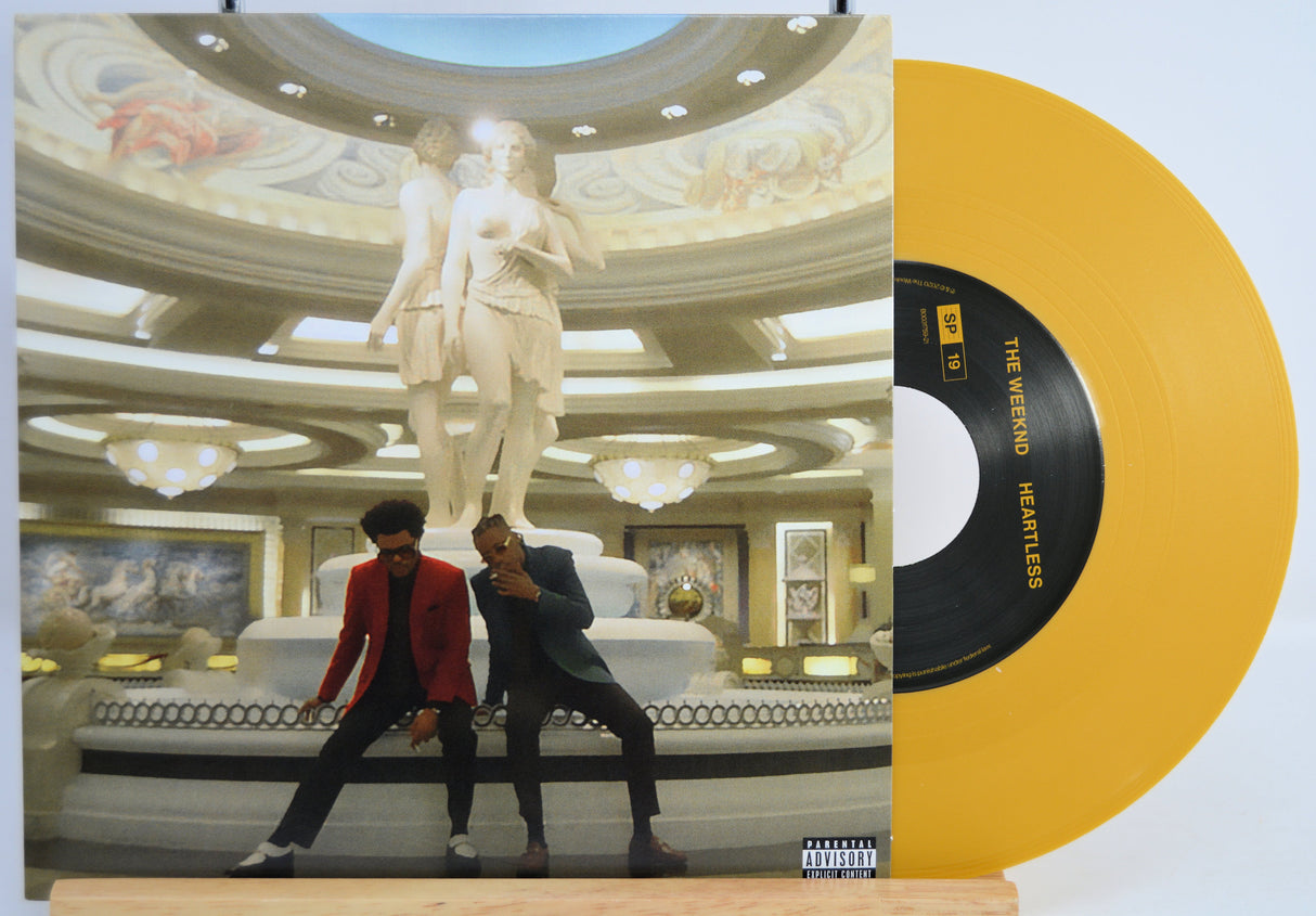 The Weekend Heartless variant #13 7 Inch Vinyl record with a black front cover featuring a person wearing sunglasses and a red jacket in front of a statue and a yellow record inside.