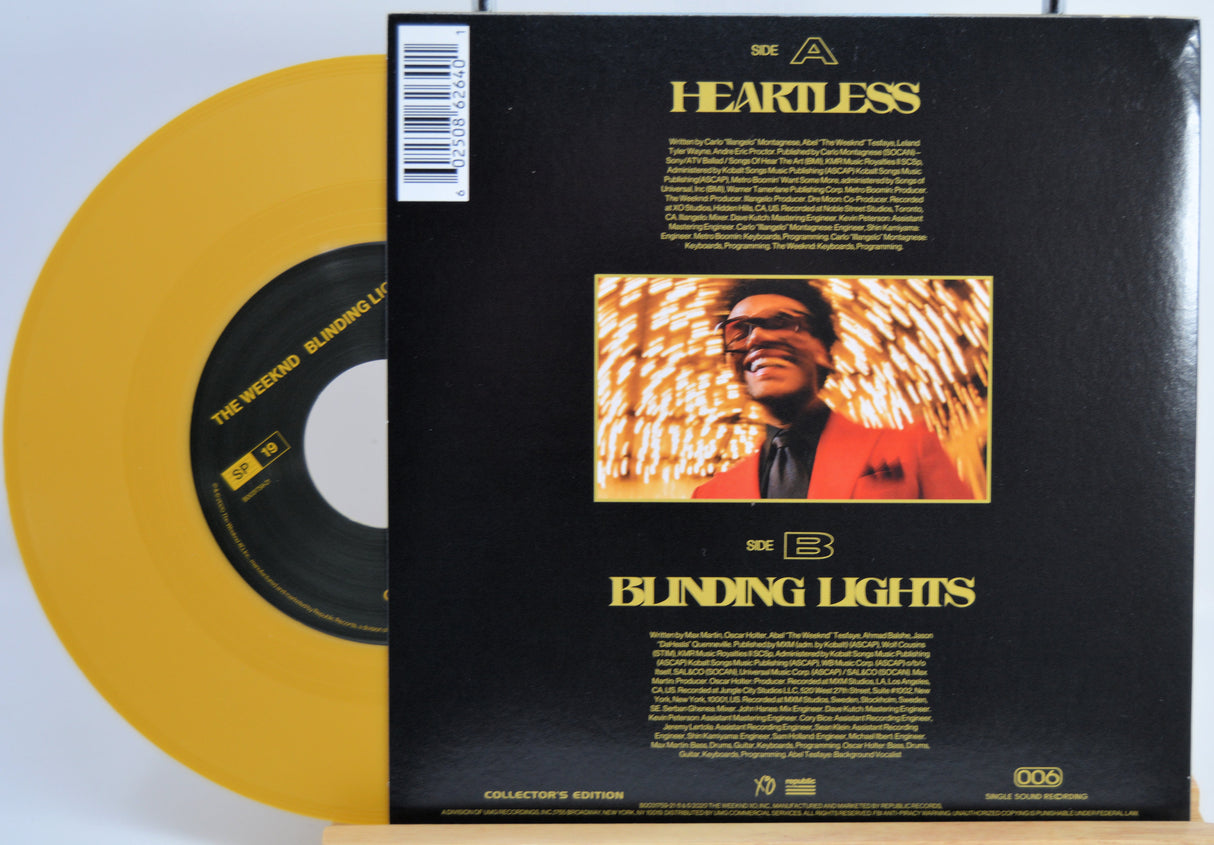 The Weekend Heartless variant #13 7 Inch Vinyl record with a black back cover featuring a person wearing sunglasses and a red jacket in front of a statue and a yellow record inside.