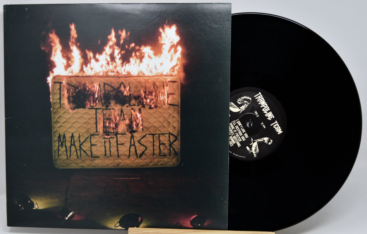 Vinyl record album with the cover partially pulled from the sleeve, showing a black record and a printed cover featuring flames over a textured gold square with the text 'IN A TIME TEAM MAKE IT FASTER'.