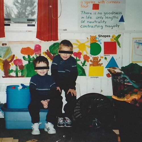 Two children in a classroom sitting in front of colorful art and educational posters