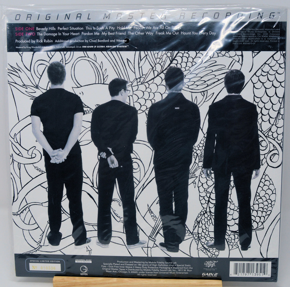 The back cover of the vinyl record 'Original Mystery Reptile' by the band EAGLE, featuring a black and white illustration of four men in suits from behind against a patterned background.
