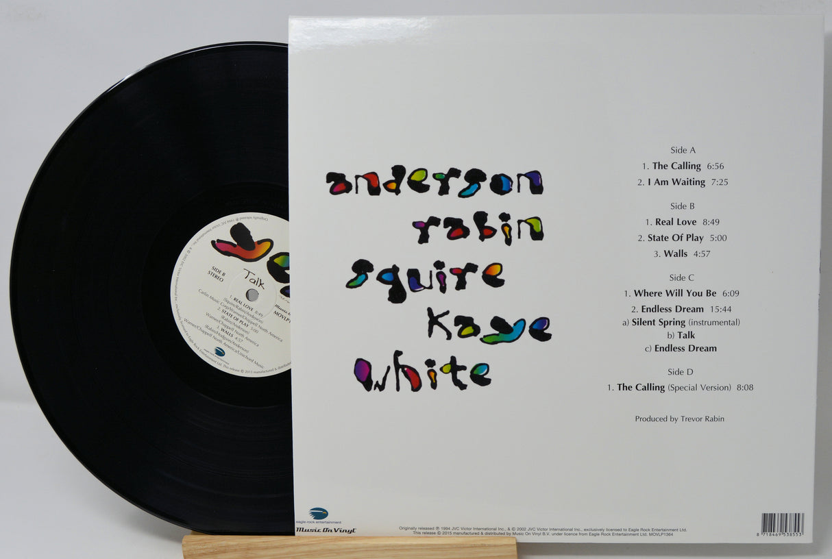 Vinyl record album shown with the black record partially visible on the left and the white outer sleeve on the right, displayed upright on a small wooden stand against a light gray background.