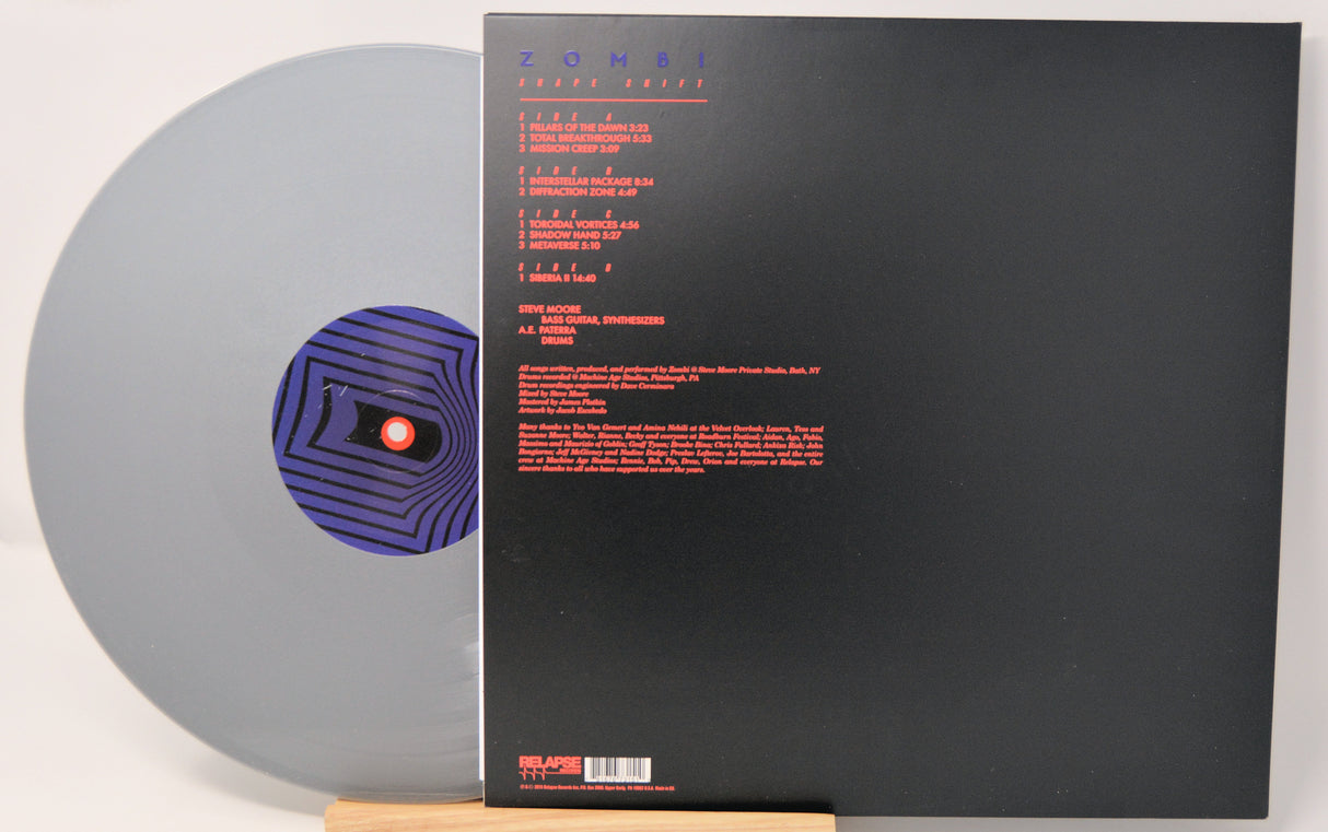 Silver vinyl record by Zombi called 'Shape Shift' and back cover with red text on a black background.