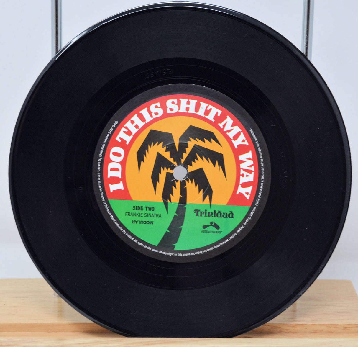 A 7-inch record with a label featuring text and a palm tree graphic. The record is black, with a red and yellow label.