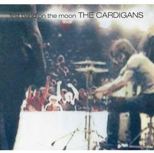Album cover for The Cardigans' First Band On The Moon featuring a grainy image of a live performance with the band and audience.