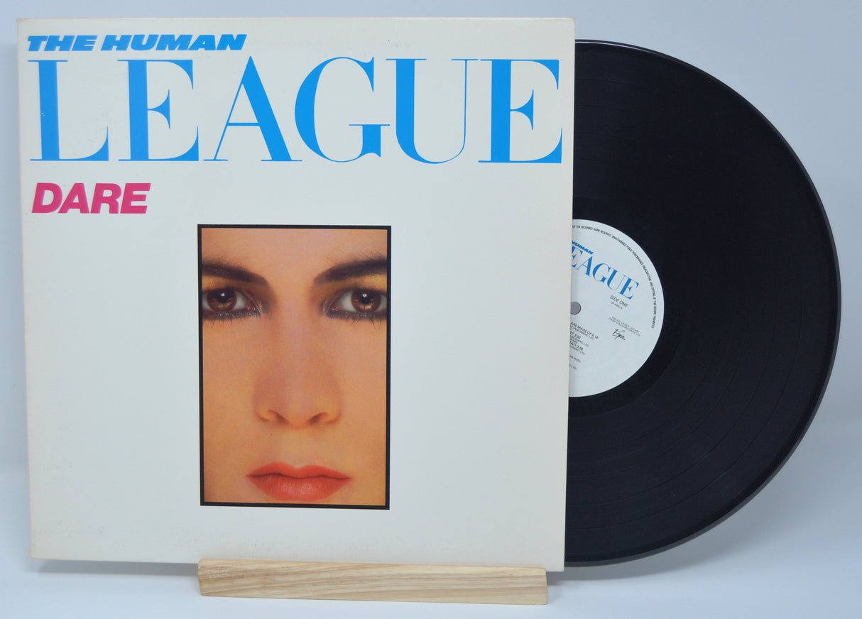 The image shows the cover of a vinyl record album titled 'Dare' by The Human League. The album cover features a close-up photograph of a woman's face, predominantly in shades of white and blue, with the band's name in bold letters.
