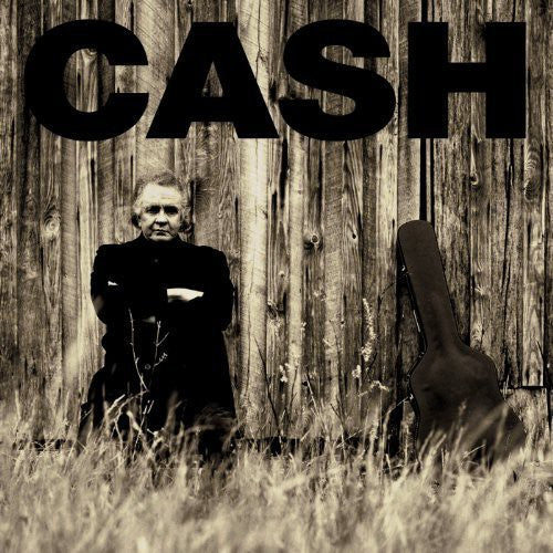 Black and white album cover titled 'American II: Unchained' featuring Johnny Cash sitting with his arms crossed in front of a wooden fence with a guitar beside him.