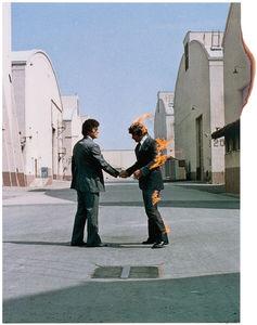Album cover for Pink Floyd's Wish You Were Here featuring two men shaking hands in an urban setting, with one of them having fire effects on his hair and clothes.
