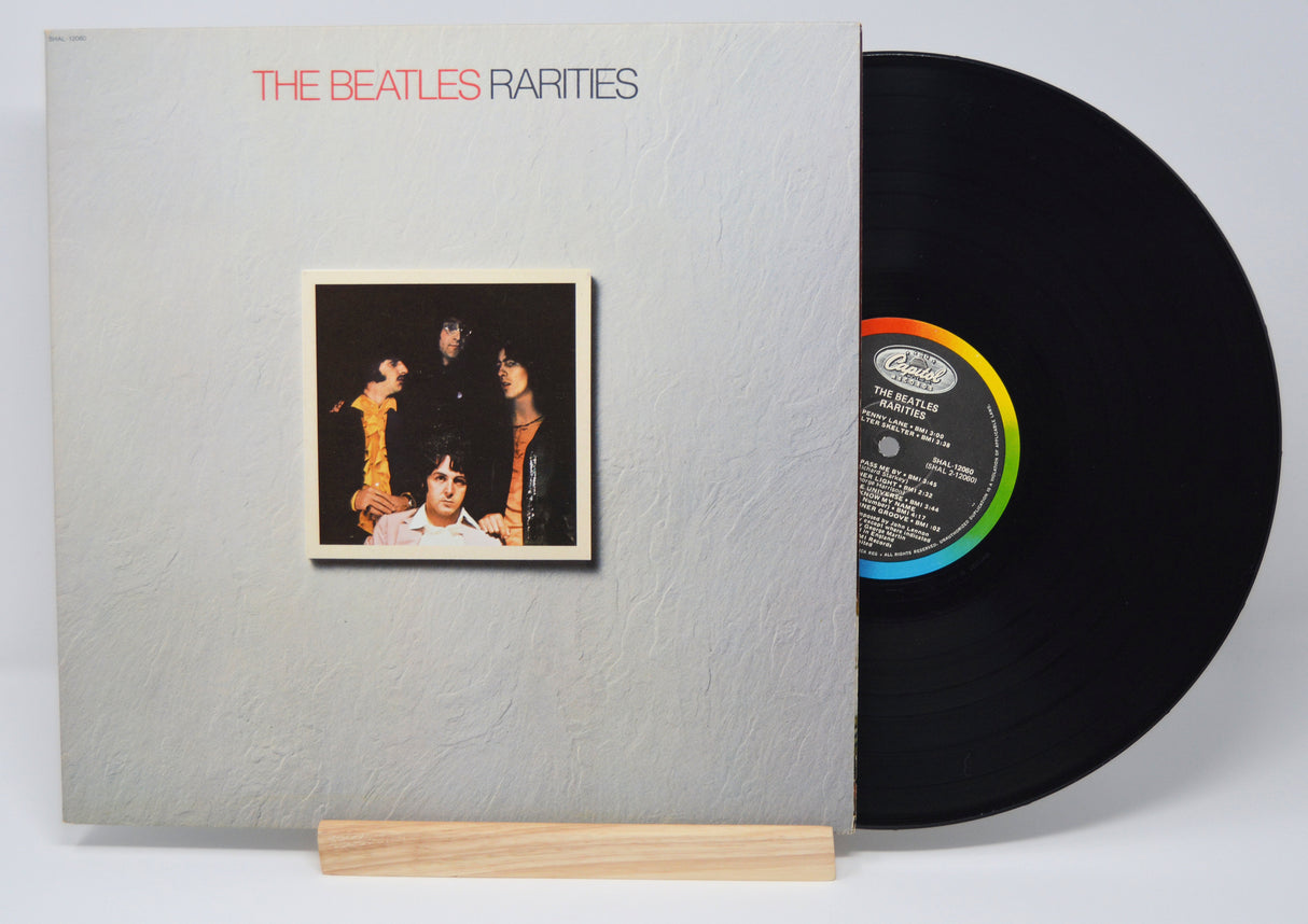 The image shows a vinyl record titled 'The Beatles - Rarities' placed in its cover sleeve, with a wooden record holder underneath.