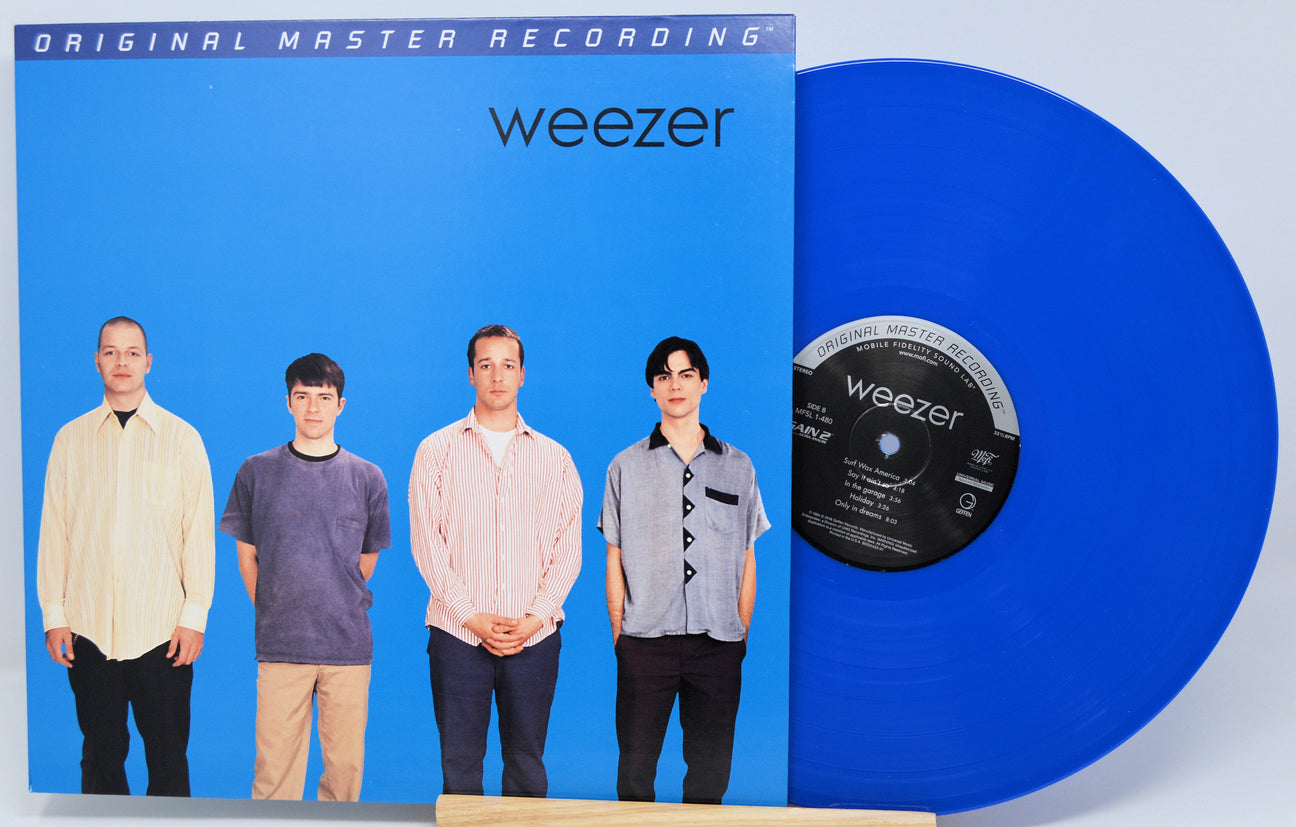 Weezer 'Blue' vinyl record album with the blue LP partially pulled from the sleeve, photographed against a light gray studio background.