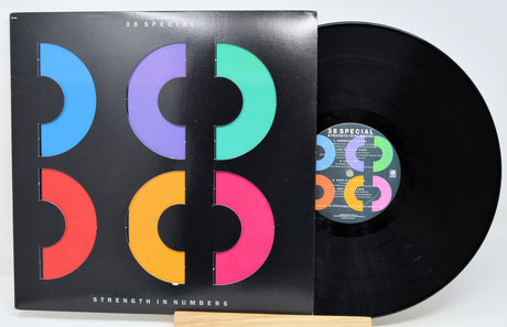 A vinyl record and its album cover for 38 Special's 'Strength in Numbers'. The black LP record is partially pulled from the sleeve, which features a black background with large, colorful geometric letterforms in blue, purple, green, red, orange, and pink.
