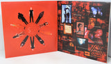 An open art book or magazine spread, showing a bright red left page with circular cutout figures and a dark collage-style right page filled with black, red, and blue imagery.