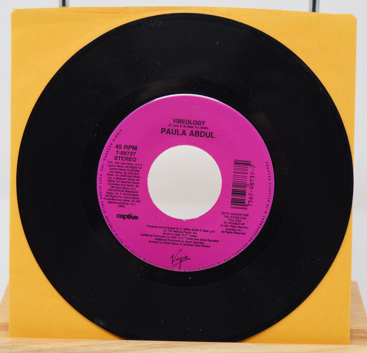 A vinyl record of Paula Abdul's album 'Vibeology' with a pink label on a yellow background.