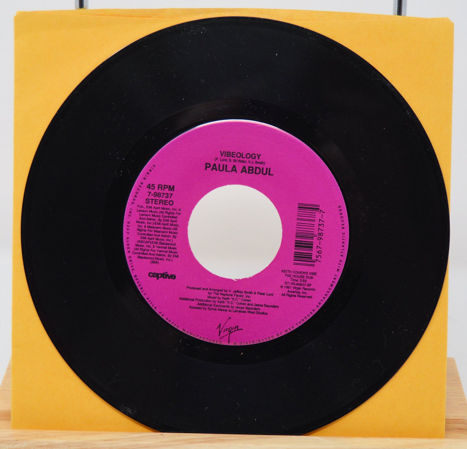 A vinyl record of Paula Abdul's album 'Vibeology' with a pink label on a yellow background.