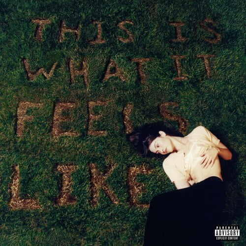 An album cover featuring a person lying on grass with the text 'THIS IS WHAT IT FEELS LIKE' arranged in large letters behind them.