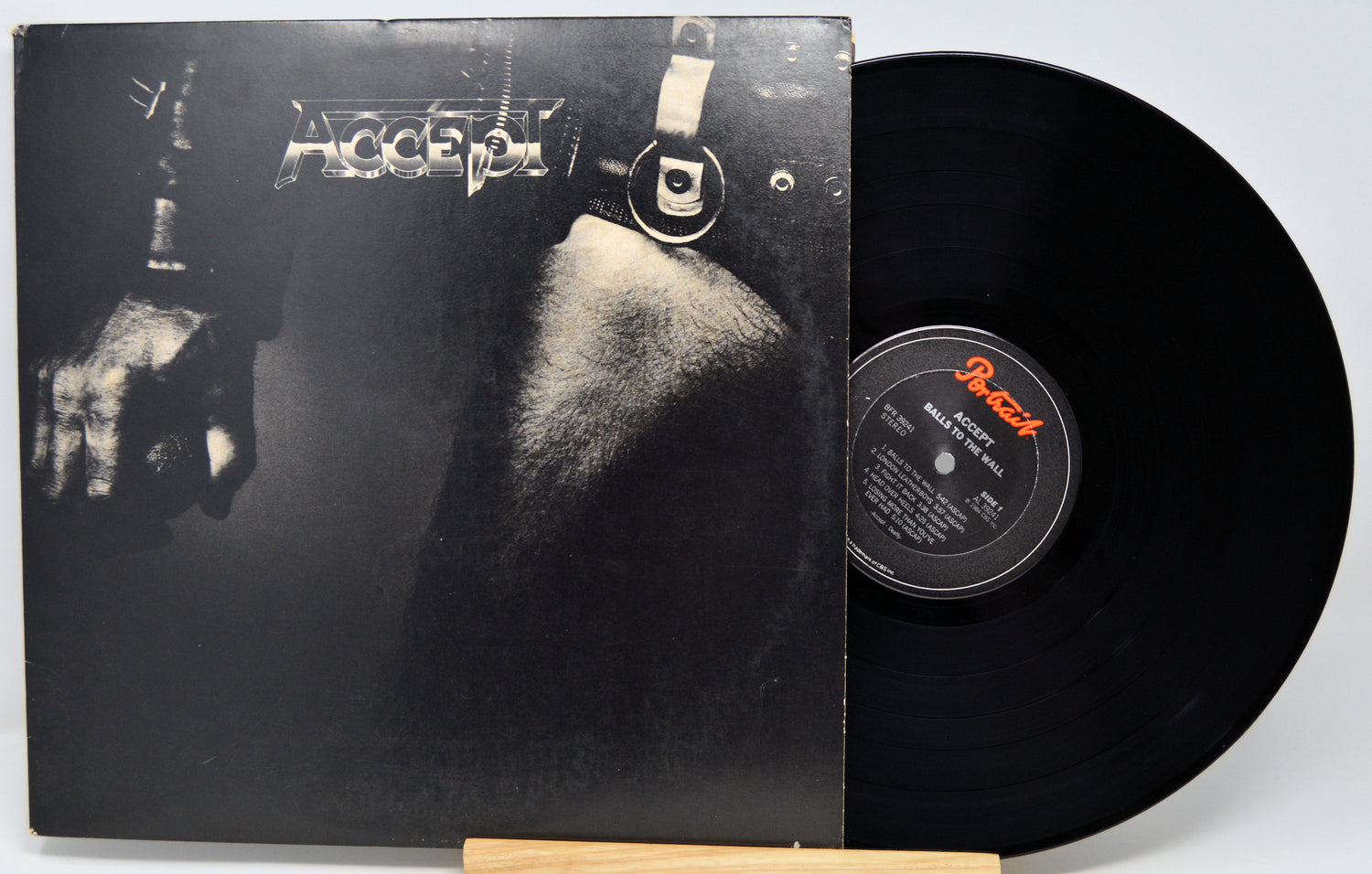 Accept's 'Blind Gaze' vinyl record LP with its black cover art sleeve and a black vinyl record partially pulled out, displayed on a small wooden stand against a light gray background.