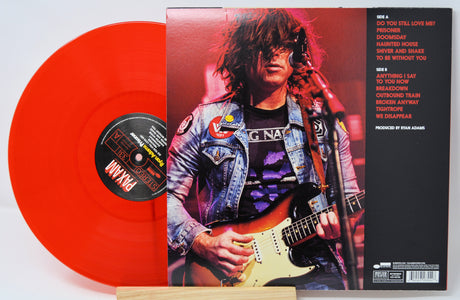 Vinyl record with red disc and cover featuring a person playing guitar, on a white background.