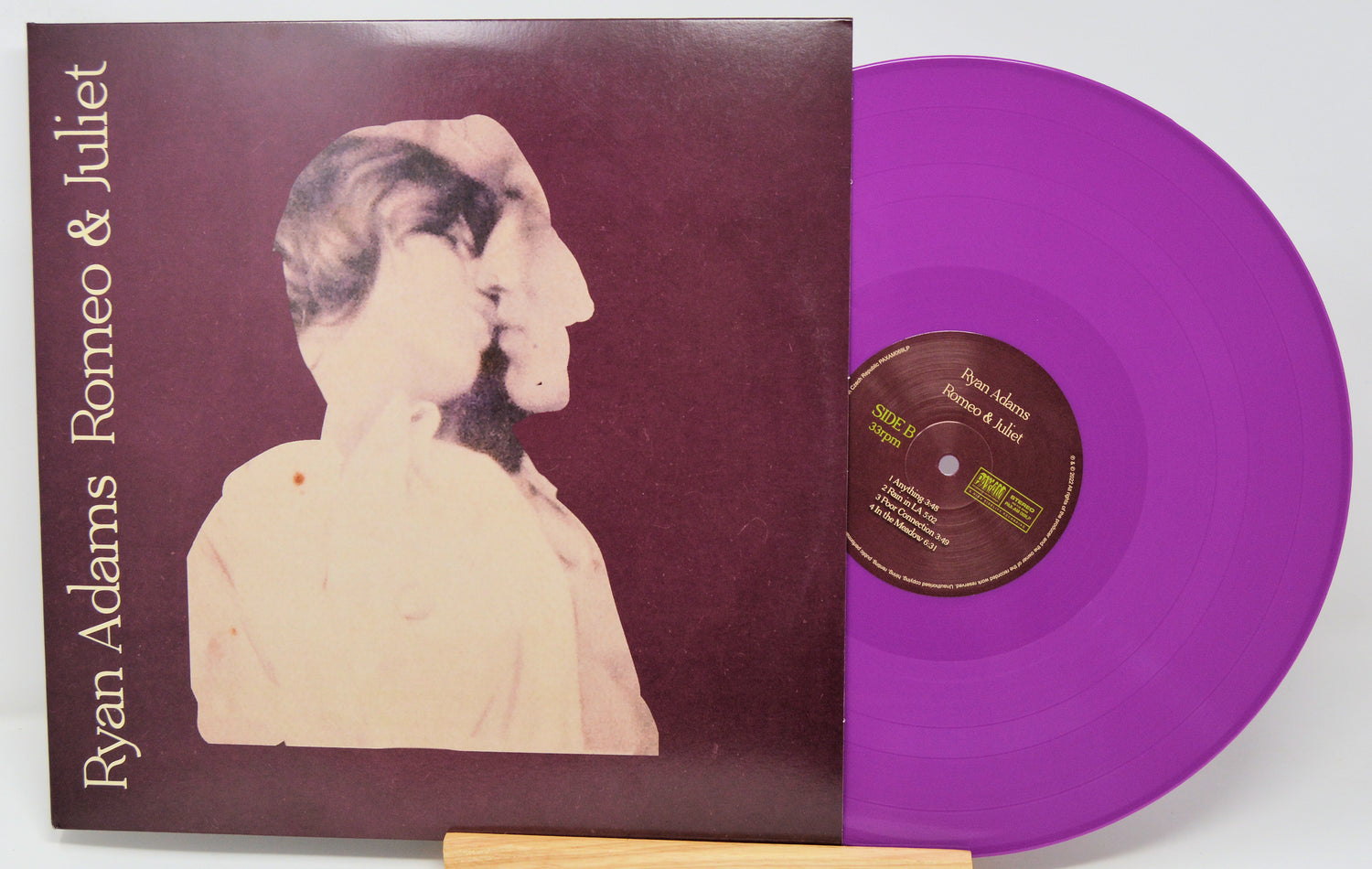 Purple vinyl record with cover featuring a stylized illustration of two faces, titled 'Romeo & Juliet' by Ryan Adams.
