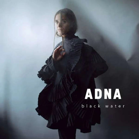 Person wearing a dark, ruffled outfit with 'ADNA black water' text on a gray background