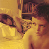 Two children lying on a bed in a bedroom setting with books in the background.